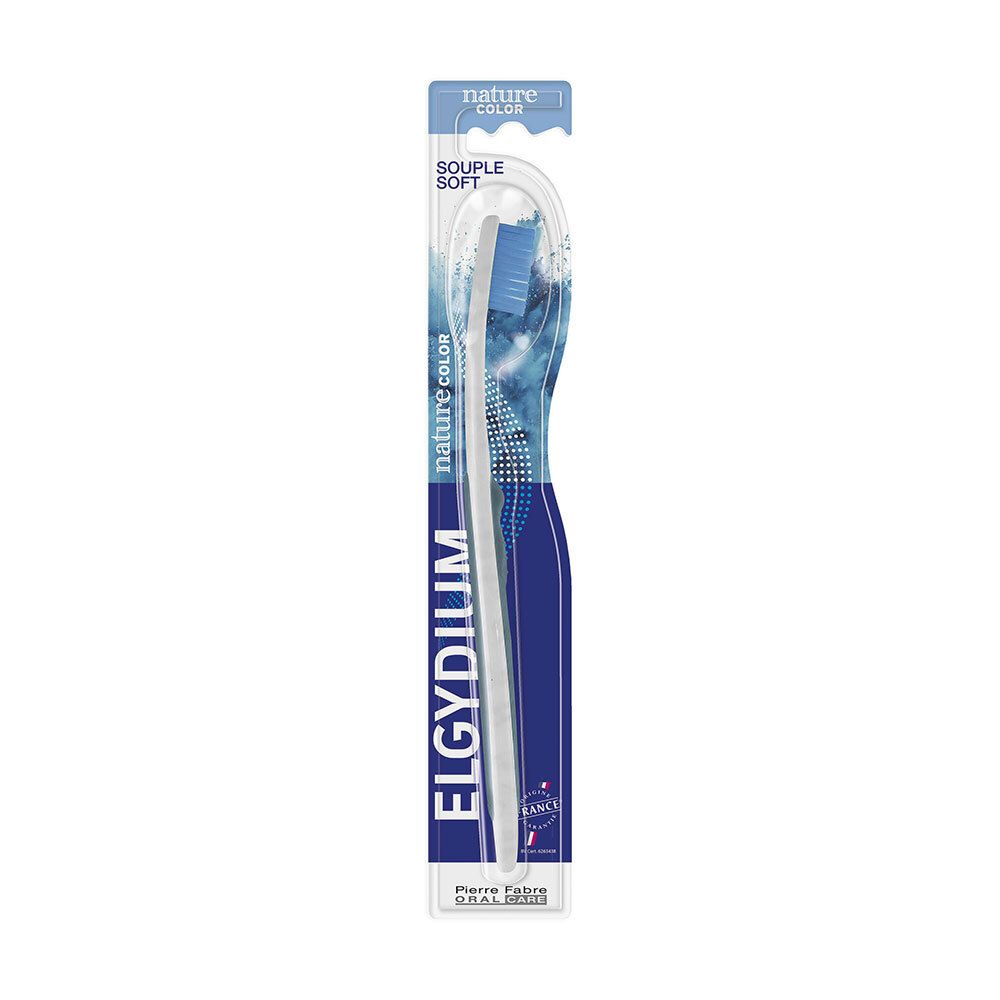 Brosse à dents dans son emballage. Manche blanc, tête de brosse bleue. Marque ELGYDIUM, texte NATURE COLOR.