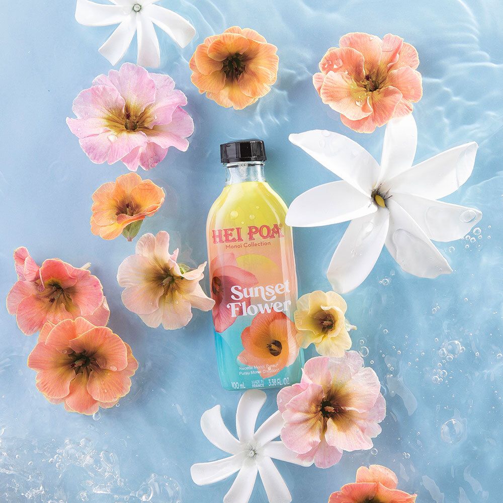 Flasche HEI POA Monoi Sonnenuntergang Blume im Wasser, umgeben von Blumen. Florales Arrangement.