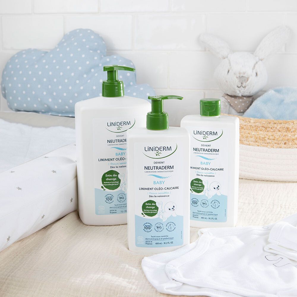 Trois flacons avec pompe verte. Inscriptions : LINIDERM, NEUTRADERM BABY. Sur un matelas à langer et à côté de jouets.