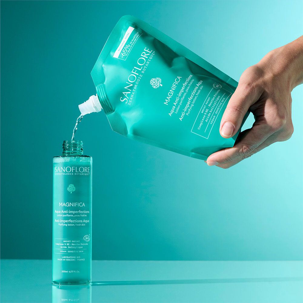 Main versant du liquide d'une recharge dans un flacon. Inscription: SANOFLORE, Magnifica.