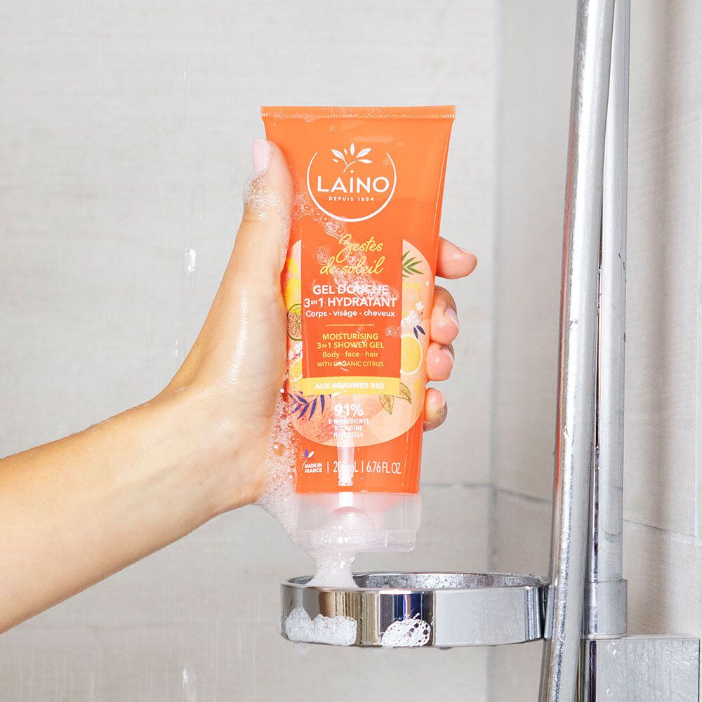 Hand hält eine LAINO Dusch-Shampoo 3in1 Zitrusfrüchte BIO Flasche unter der Dusche.