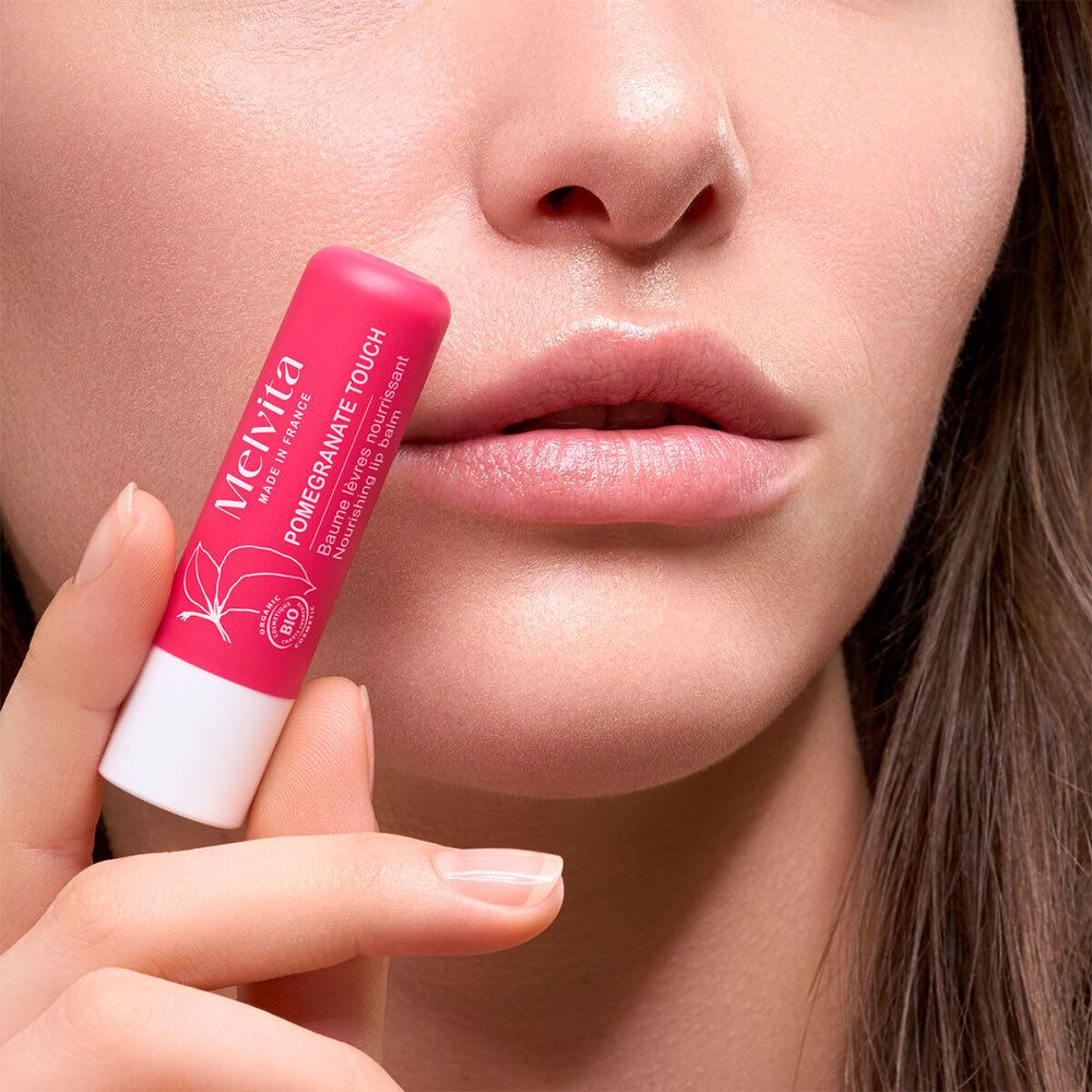 Hand hält Melvita Lippenbalsam Pomegranate Touch vor Lippen.