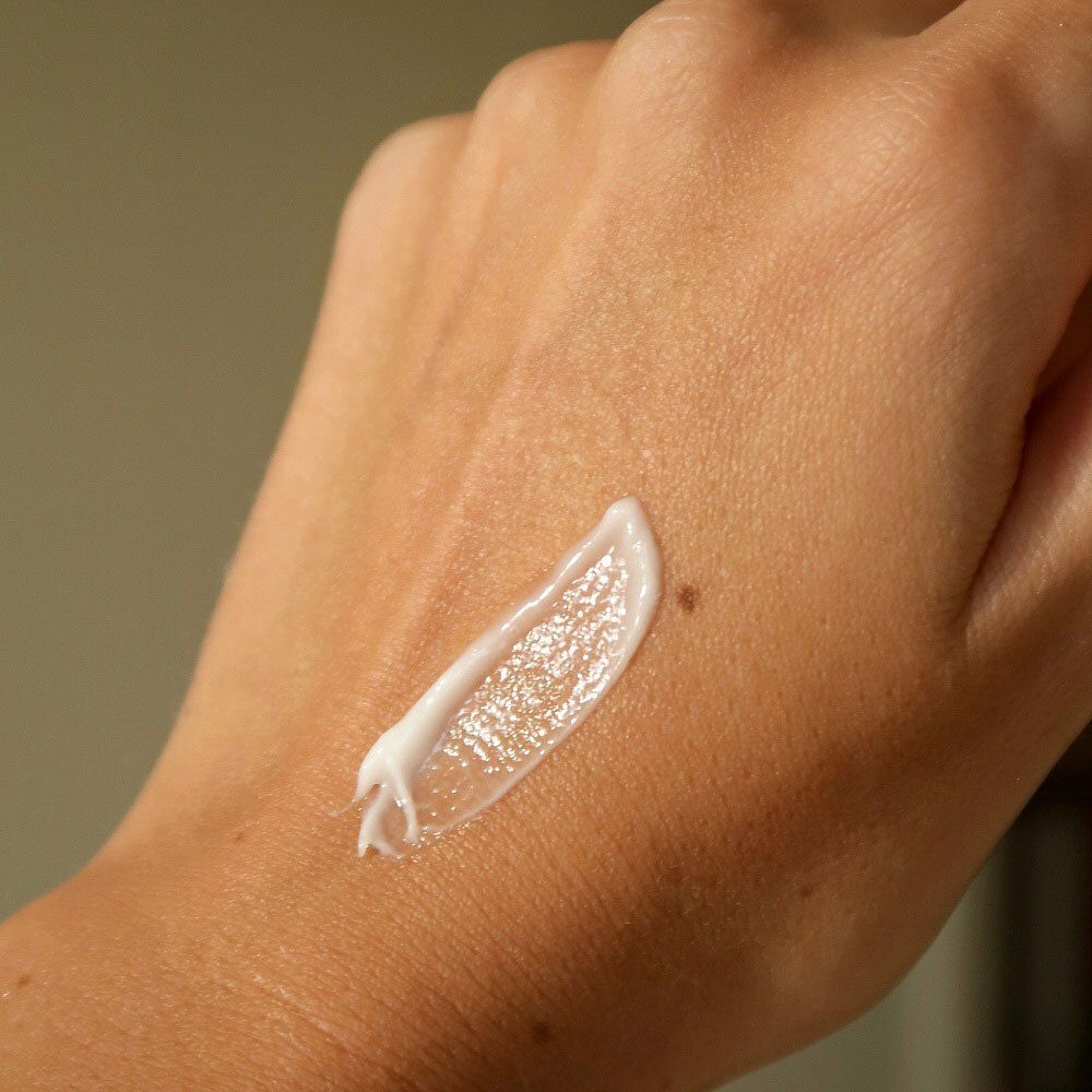 Creme-Tube auf einem Spiegel. Spiegel auf einem Holztablett. Baumwollblüten im Hintergrund.