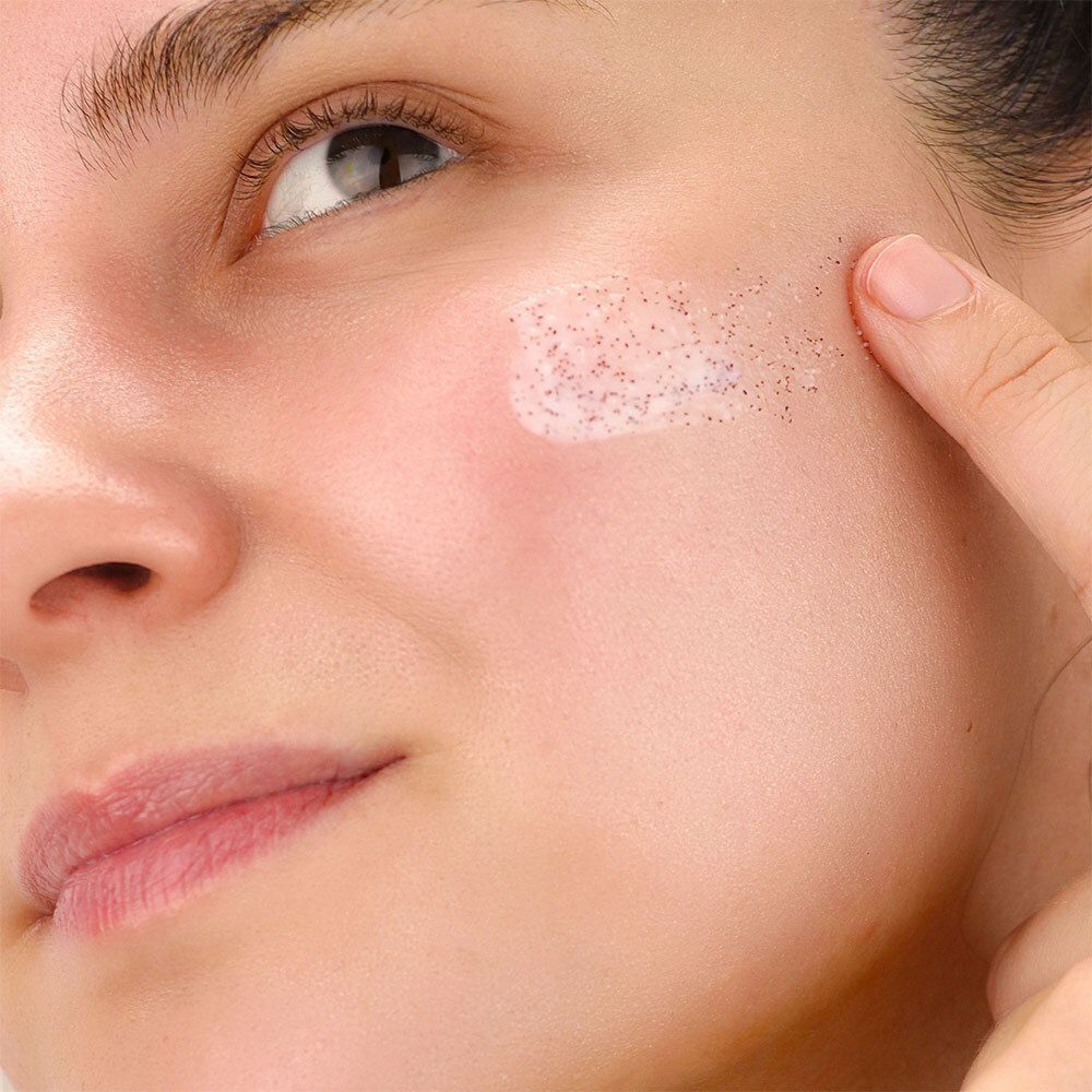 Nahaufnahme eines Gesichts. Auf der Wange wird ein Peeling aufgetragen. Die Haut ist sichtbar. 