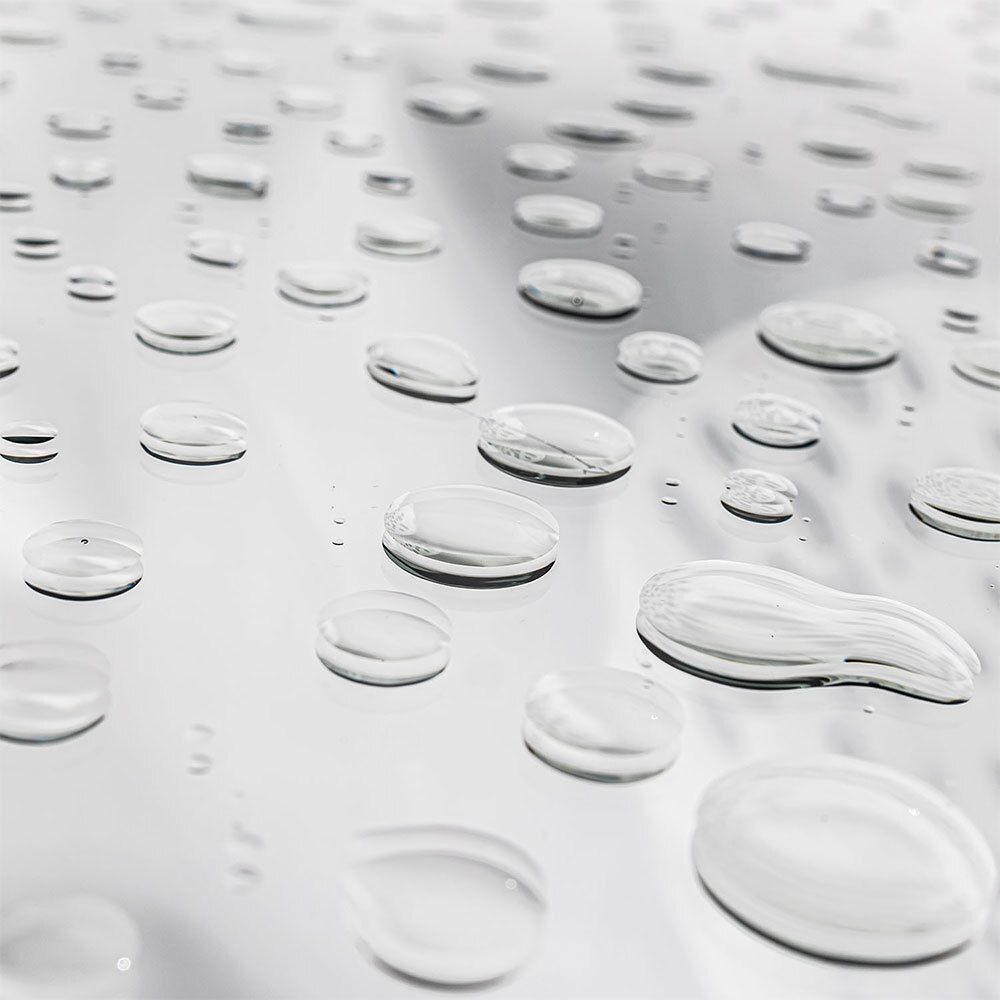 Nahaufnahme von Wassertropfen auf einer glänzenden Oberfläche. Die Tropfen sind klar und unterschiedlich groß.