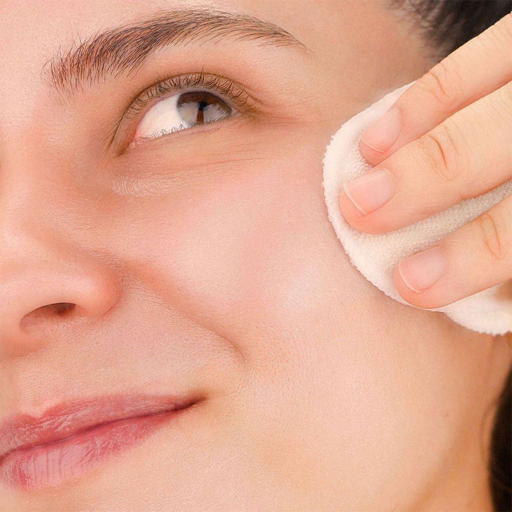 Nahaufnahme eines Gesichts, das mit einem Wattepad gereinigt wird. Die Haut ist sichtbar.