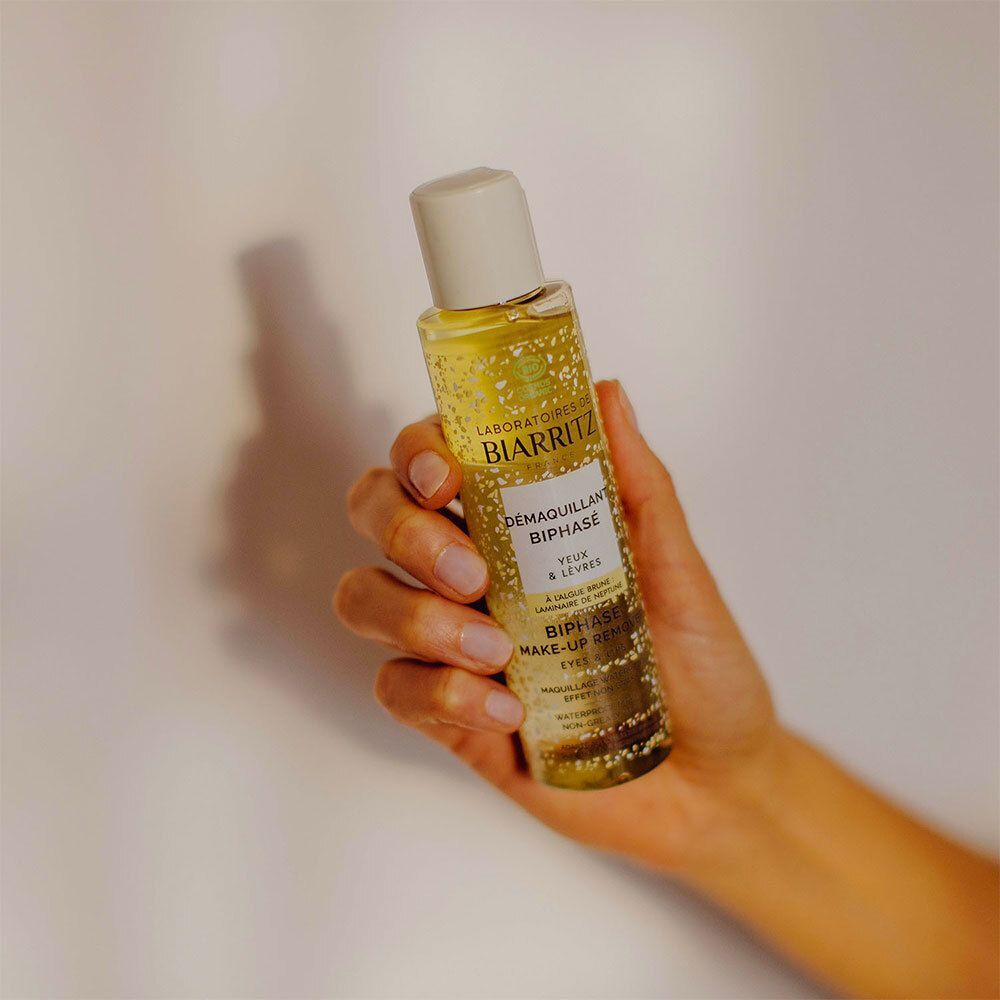 Eine Hand hält eine Flasche Démaquillant Biphasé Yeux & Lèvres Bio. Der Hintergrund ist weiß.
