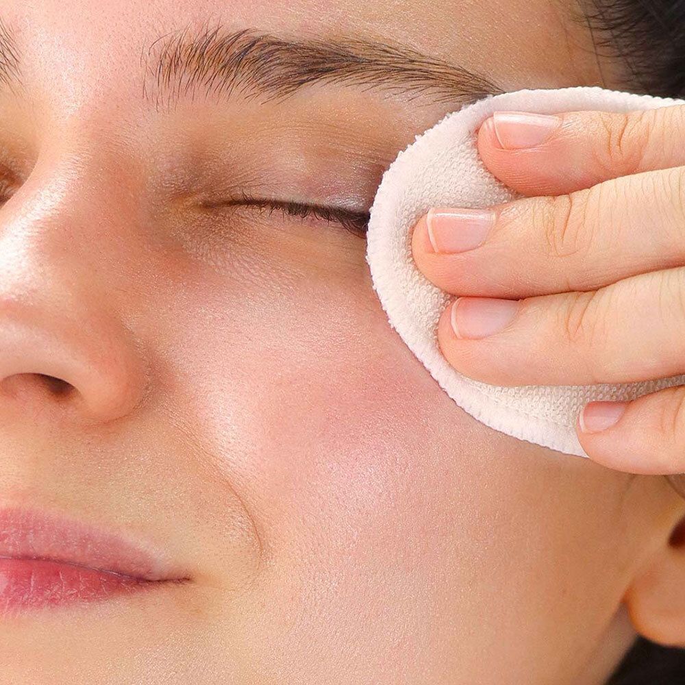 Eine Person reinigt das Auge mit einem runden Wattepad. Nahaufnahme des Gesichts.