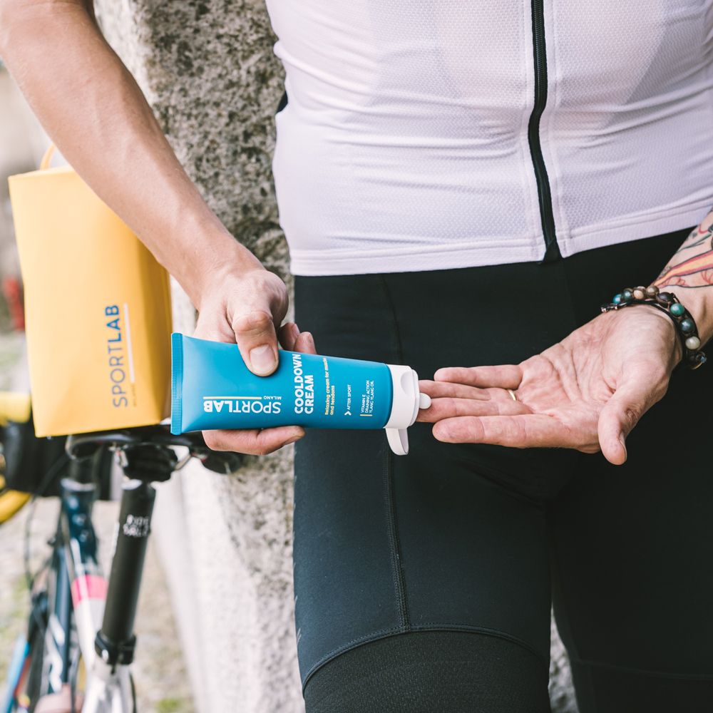Persona tiene un tubo. Testo: SPORTLAB Milano, COOLDOWN CREAM. Abbigliamento sportivo. Borsa gialla, bici sullo sfondo.