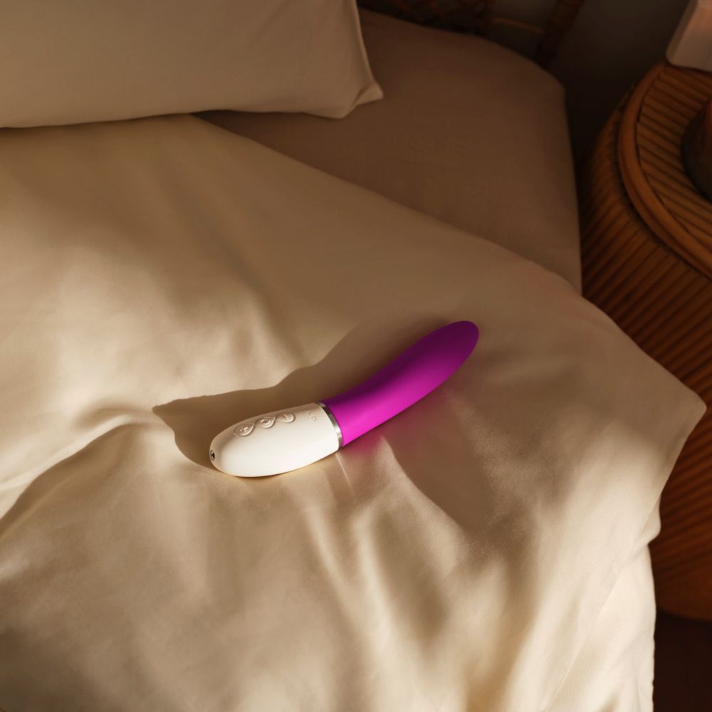 Vibrator auf Bettlaken. Lila-weiße Farbe. Liegt auf beigem Stoff.