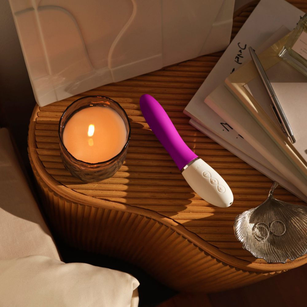 Vibrator auf Tisch. Lila-weiße Farbe. Kerze und Schmuck daneben.
