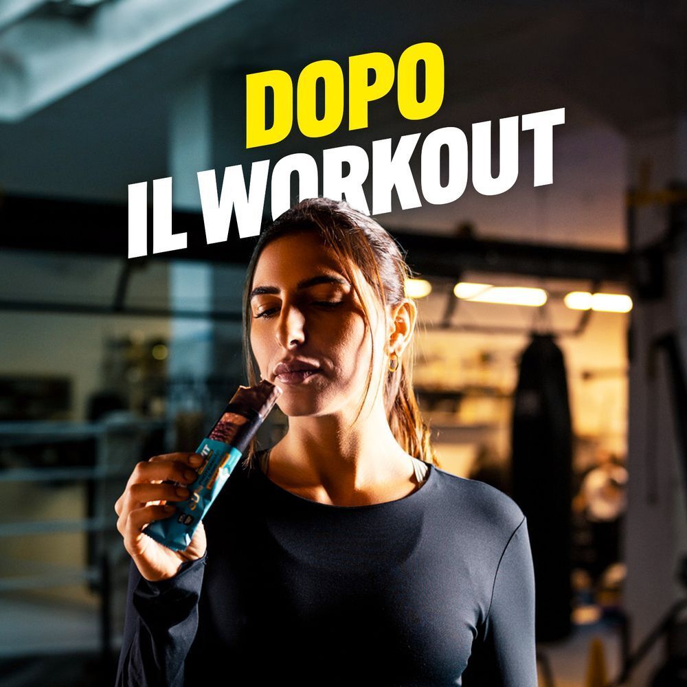 Donna mangia una barretta proteica ENERVIT Crunchy Hazelnut dopo l'allenamento.