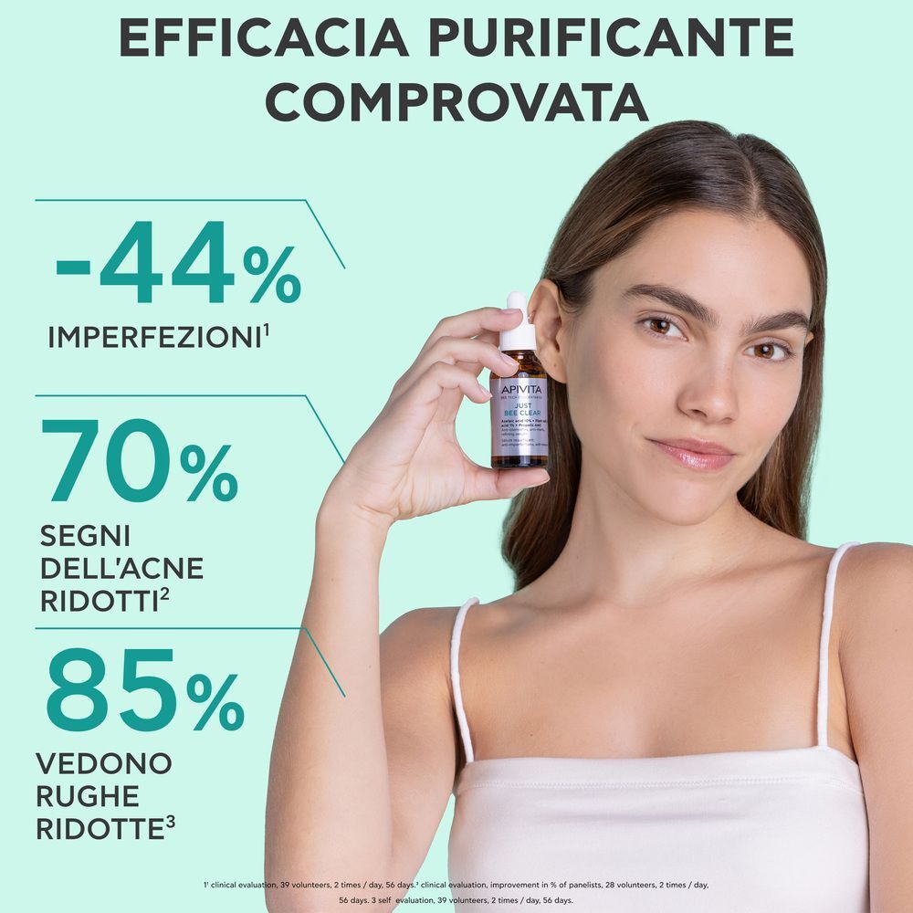 Donna tiene in mano un flacone di siero Apivita Just Bee Clear. Testo in italiano sull'efficacia.