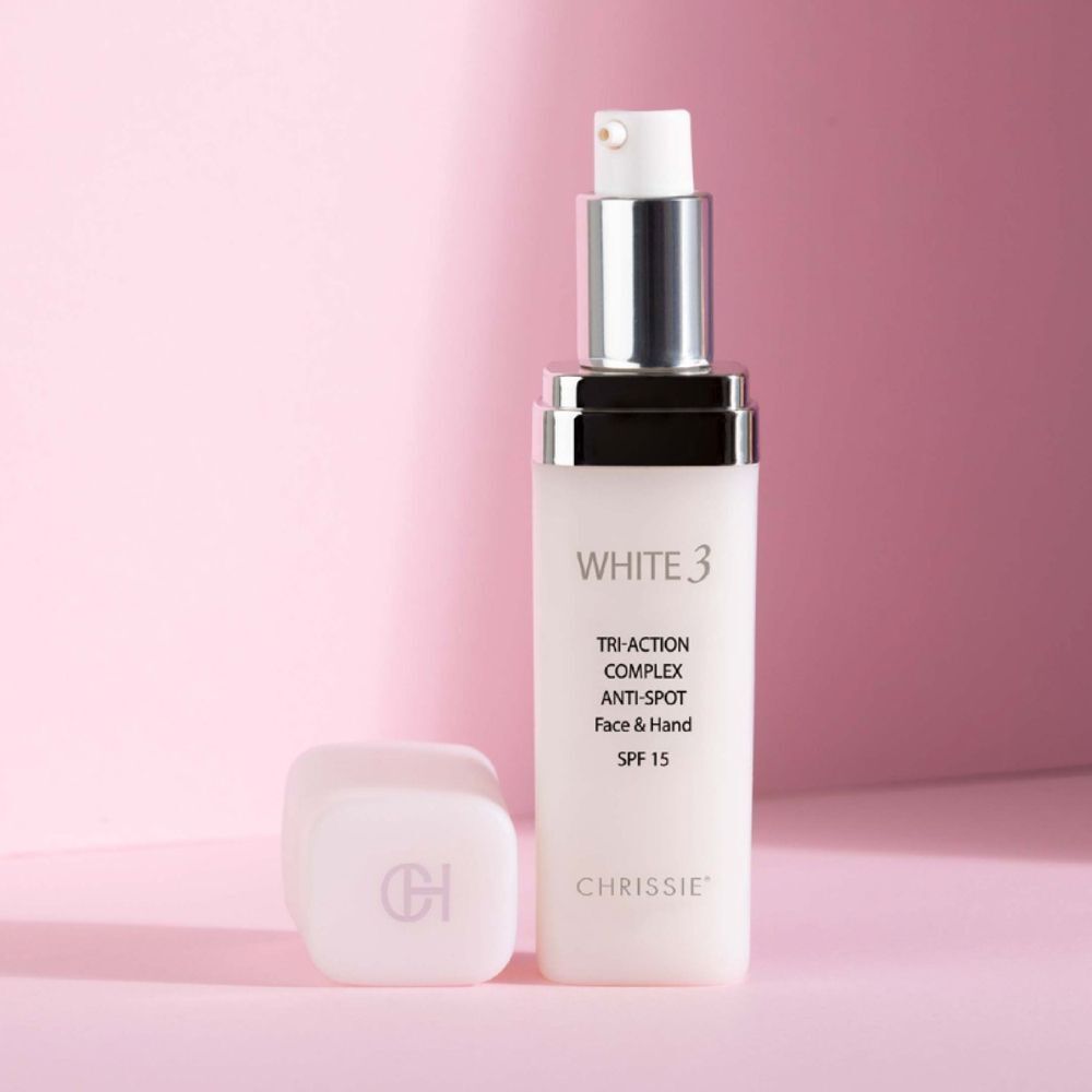 Un flacone Chrissie White 3 Tri-Action Complex Antimacchia Schiarente con tappo rimosso su sfondo rosa.