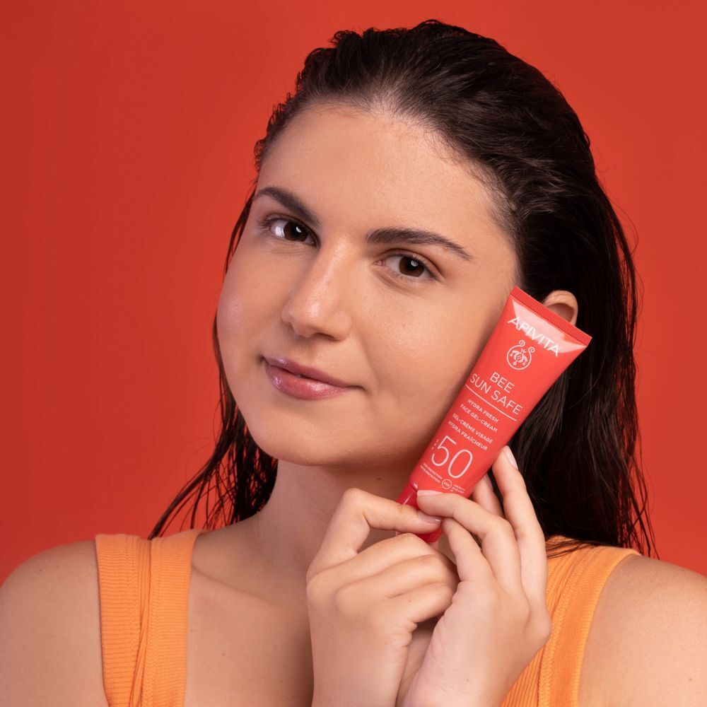 Una donna tiene un tubetto rosso APIVITA Bee Sun Safe Crema Gel Viso SPF50.
