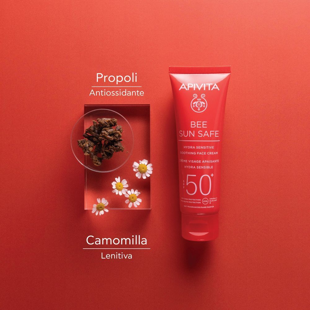 Tubo rosso di crema viso solare SPF 50+, vicino a fiori di camomilla e propoli.