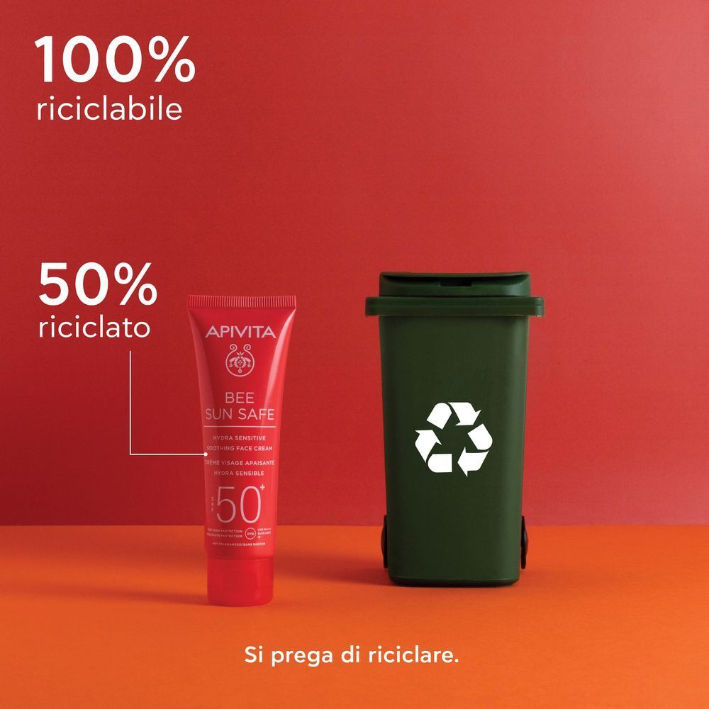 Tubetto rosso di crema solare viso APIVITA SPF 50+, accanto a un bidone verde per il riciclo.