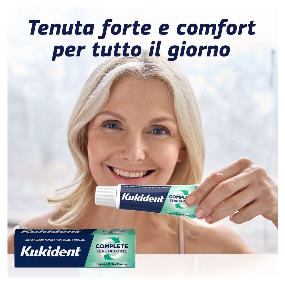 Donna sorridente che tiene in mano un tubo di crema adesiva Kukident Complete.