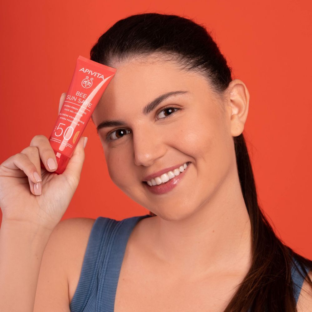 Donna che tiene un tubetto rosso di crema-gel solare APIVITA SPF 50.