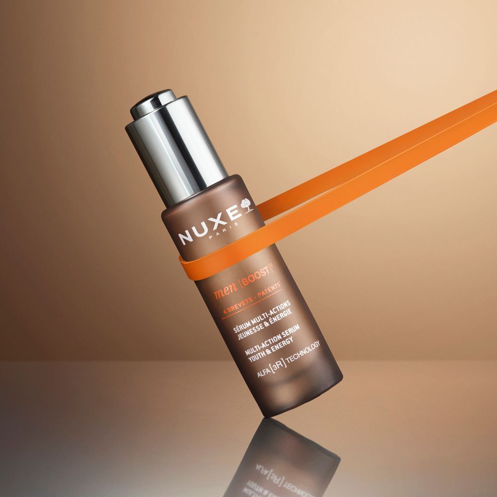 Flacone Nuxe Men anti-età con tappo contagocce, tenuto da un nastro arancione.