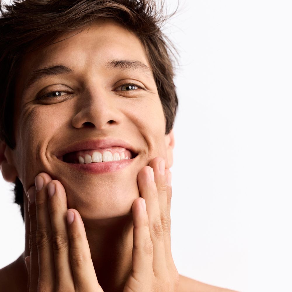 Un uomo sorridente che si tocca il viso con entrambe le mani.
