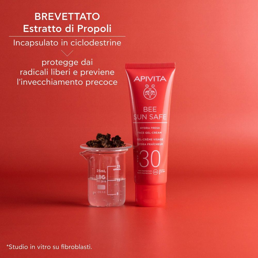 Tubetto rosso APIVITA Bee Sun Safe SPF 30 accanto a un bicchiere di vetro con estratto di propoli.