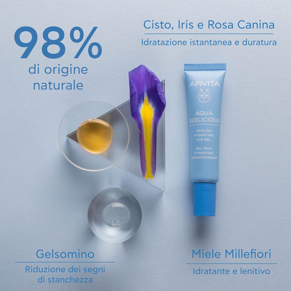 Tubetto di gel contorno occhi APIVITA Aqua Beelicious vicino a fiore di iris, miele e oggetti in vetro. 98% ingredienti naturali.
