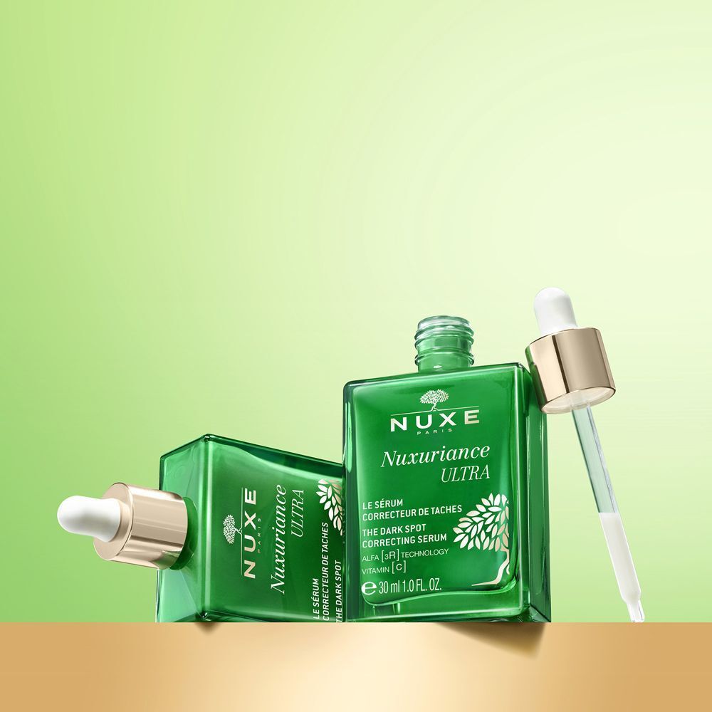 Due flaconi in vetro verde Nuxe Nuxuriance Ultra siero, uno sdraiato, uno in piedi.