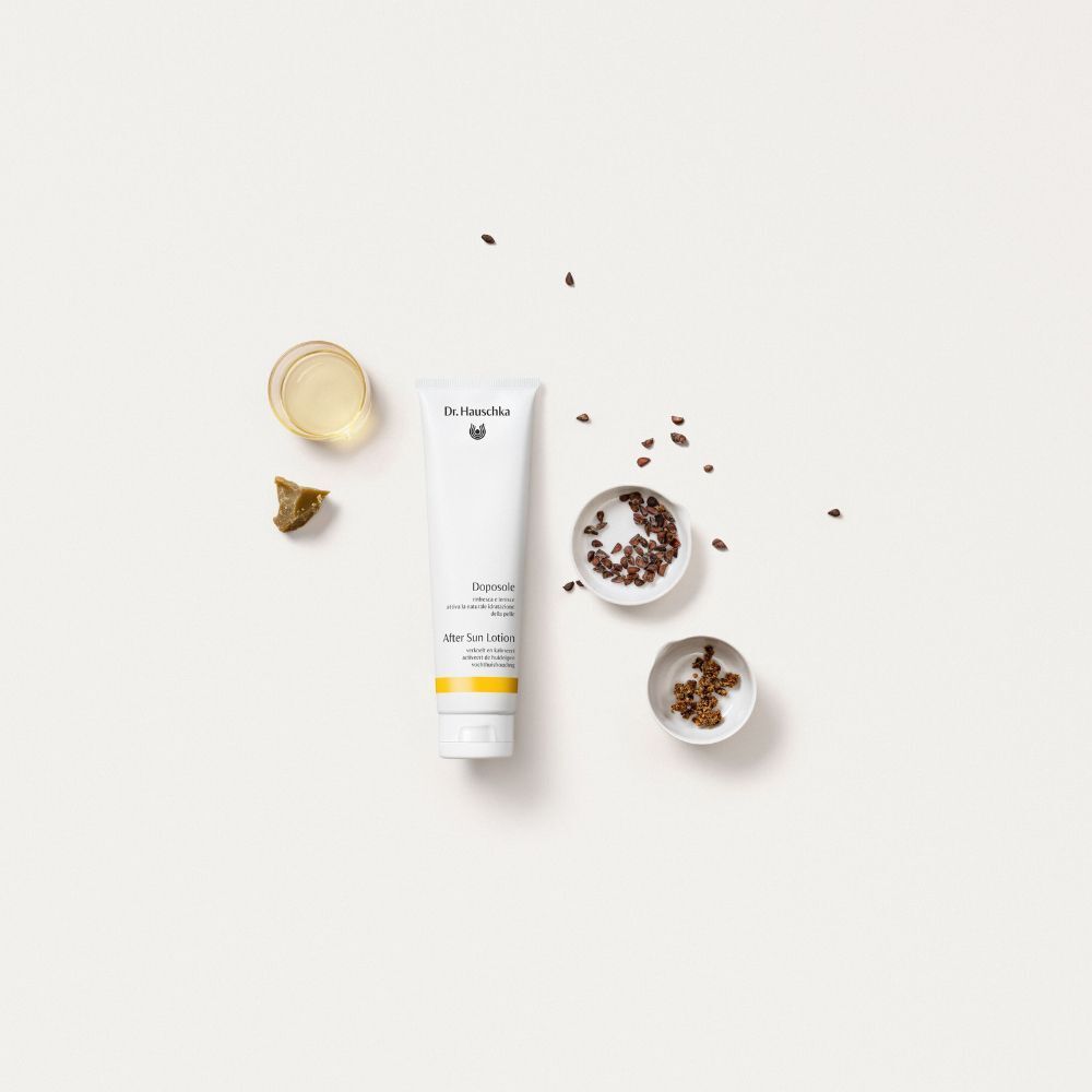Un tubetto di Dr. Hauschka Doposole After Sun Lotion circondato da piccole ciotole con semi e olio.