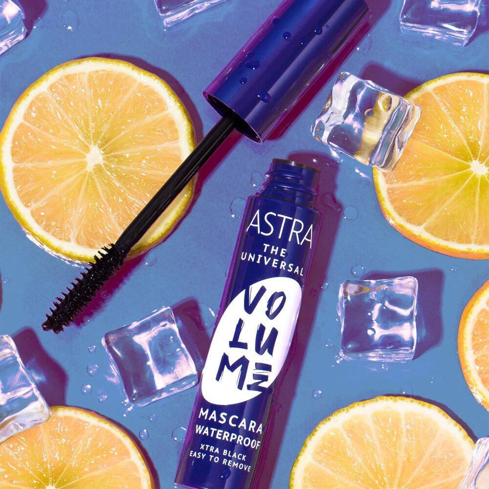 Mascara Astra Volume, waterproof, xtra black. Pennello e flacone su sfondo blu con fette di limone e cubetti di ghiaccio.