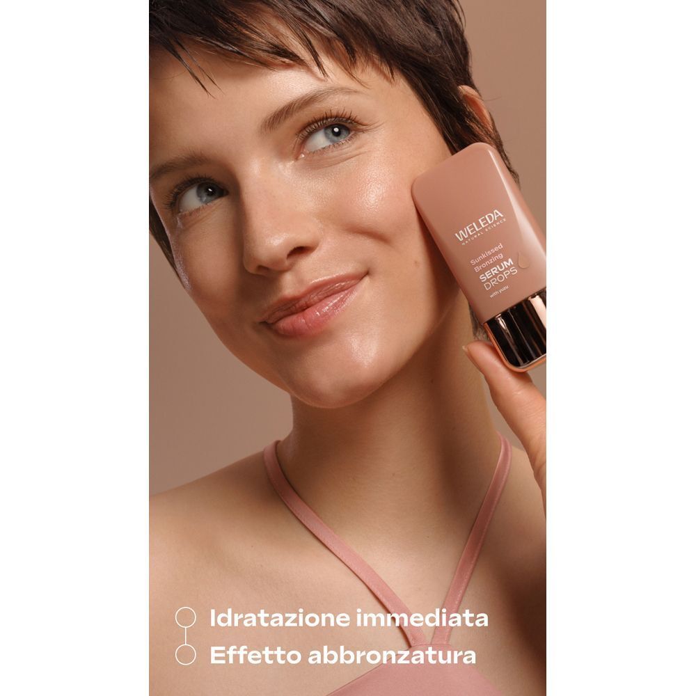 Donna tiene flacone WELEDA Sunkissed Bronzing Serum Drops vicino alla guancia.