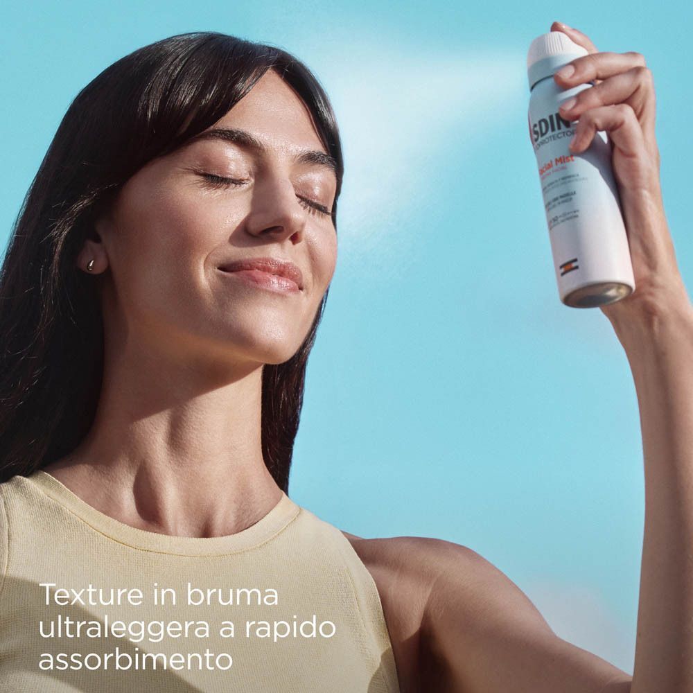 Una donna si spruzza ISDIN Fotoprotector Bruma Viso SPF 50 sul viso.