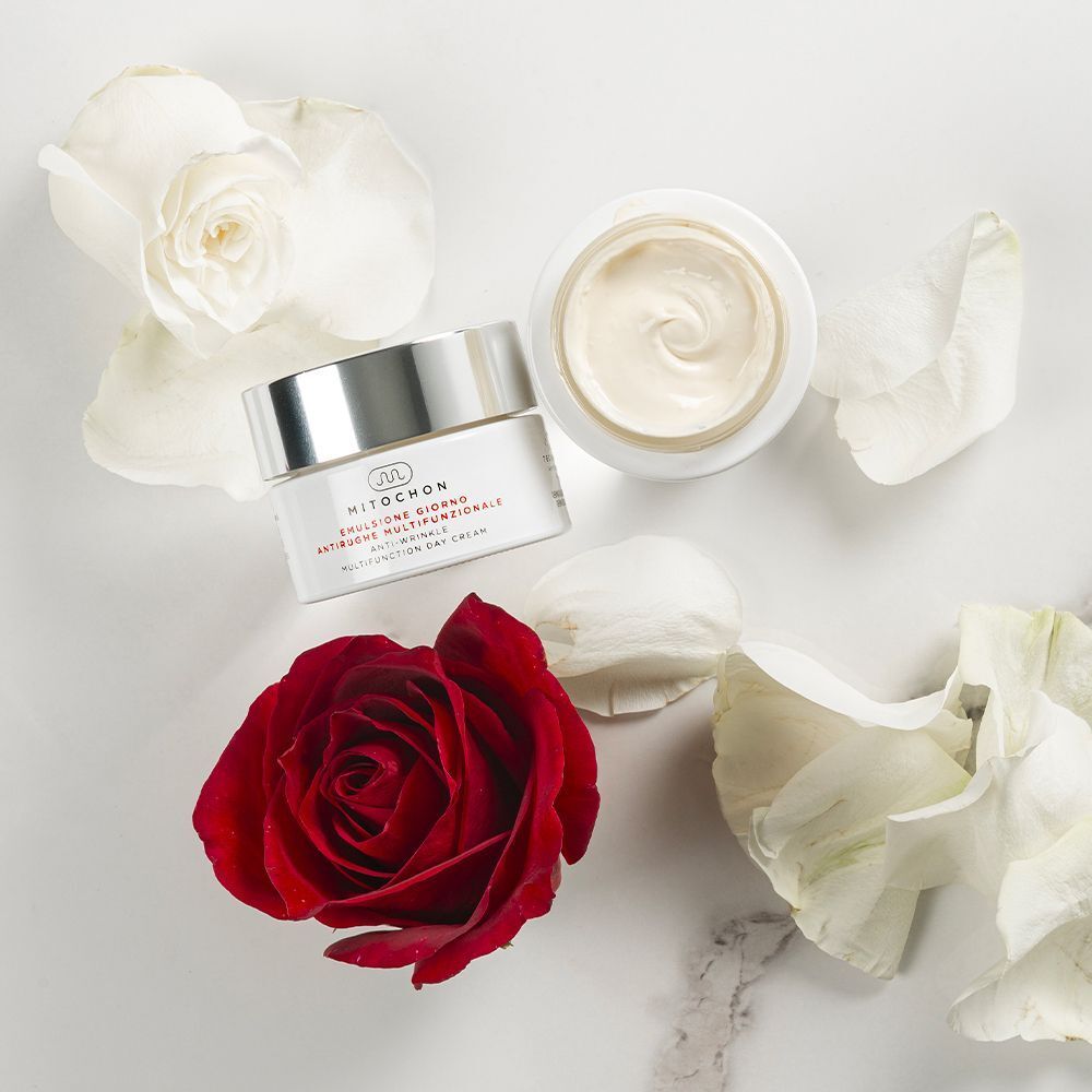 Vasetto aperto e chiuso di crema giorno multifunzionale Mitochon, circondato da petali di rosa.