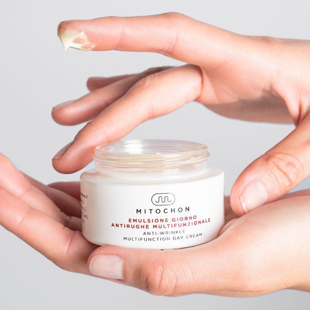 Mani che tengono un vasetto di crema giorno Mitochon aperto con crema visibile.