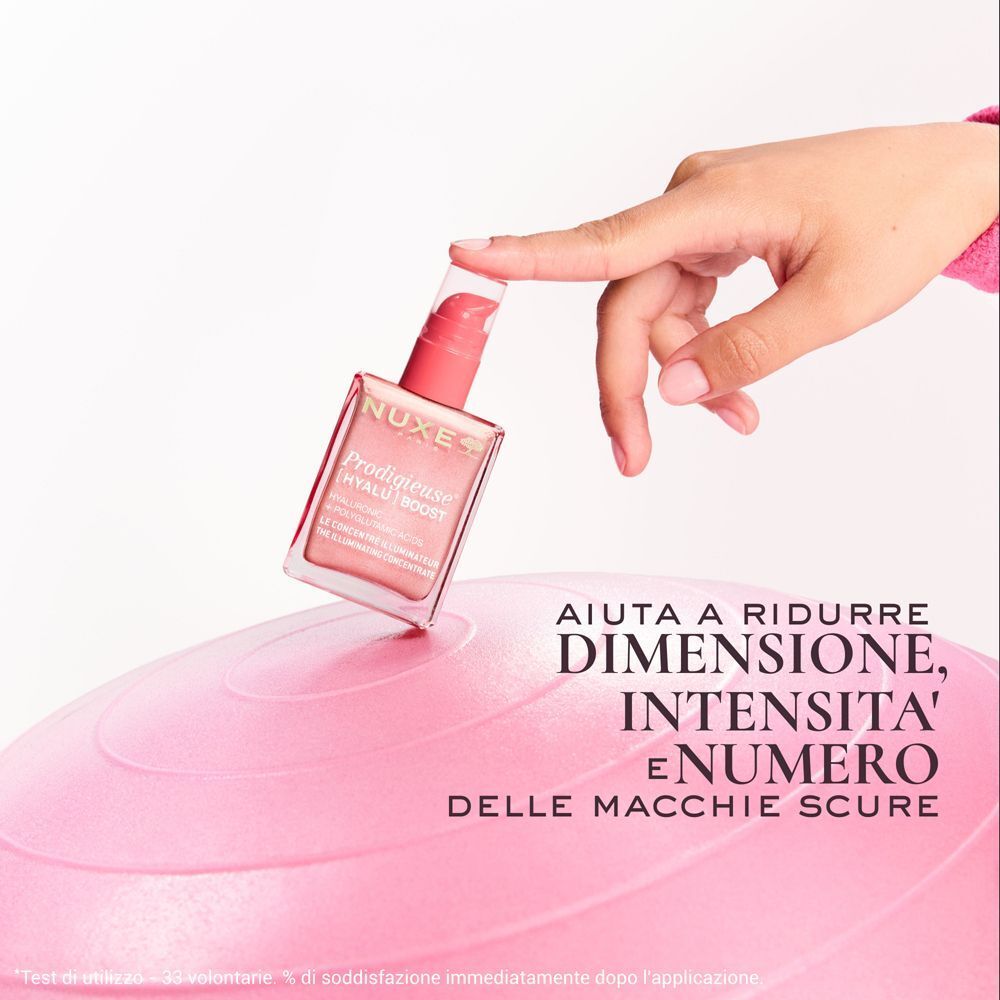 Mano che tiene un flacone Nuxe Prodigieuse [Hyalu] Boost sopra un pallone da ginnastica.