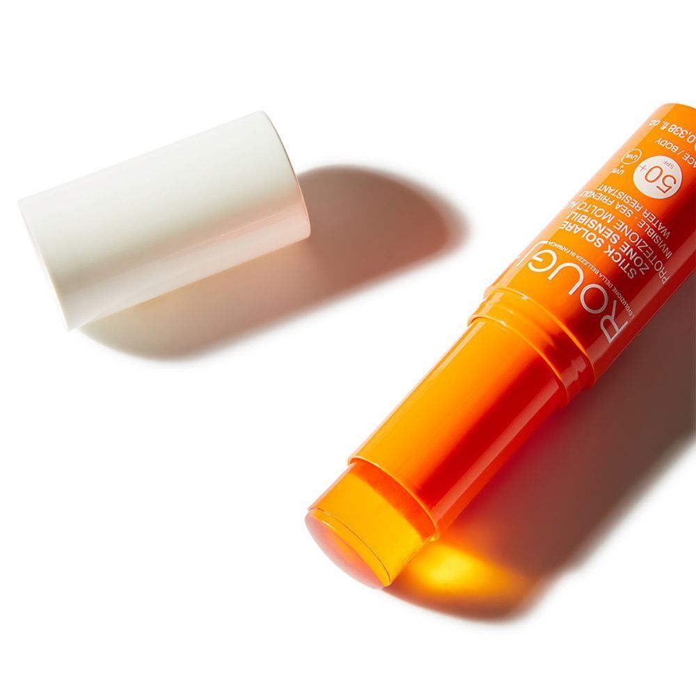 Uno stick solare arancione aperto, con il suo cappuccio bianco accanto. SPF 50.