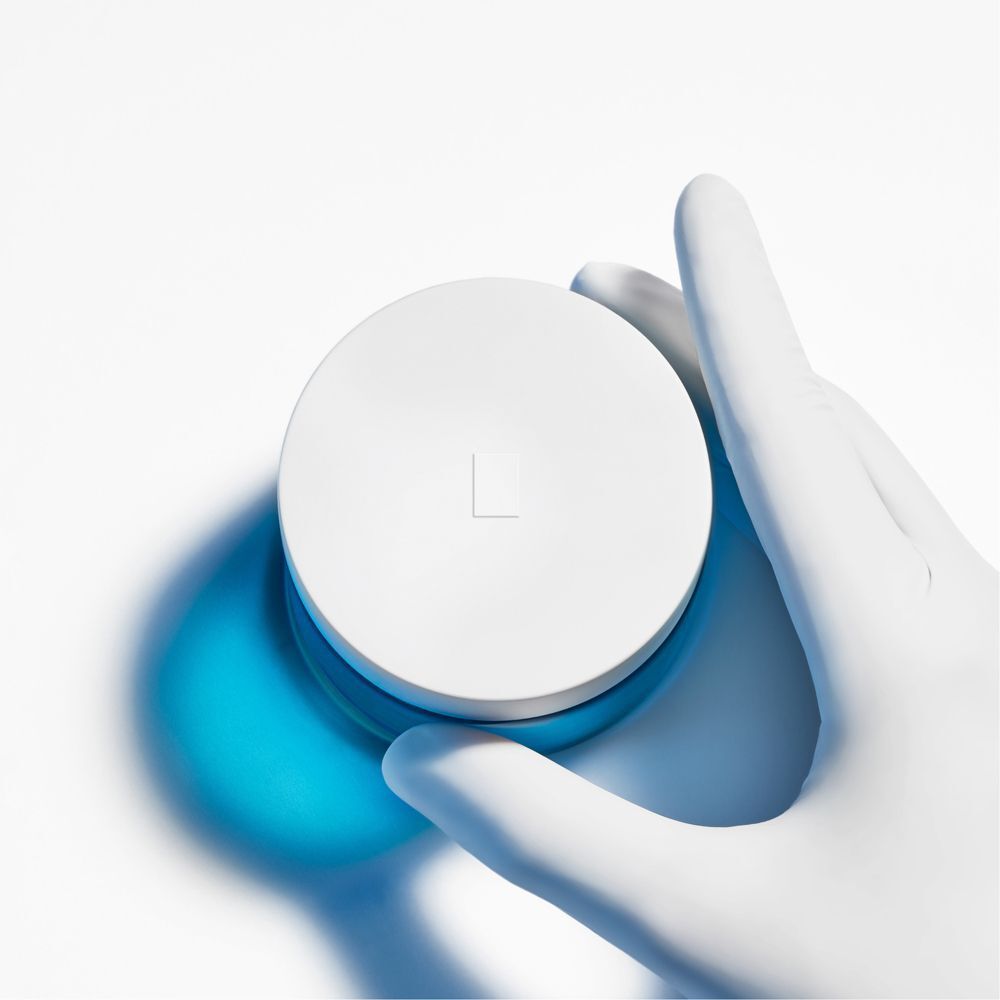 Una mano con guanto bianco tiene il coperchio di un vasetto di crema La Roche-Posay Hyalu B5 SPF30.
