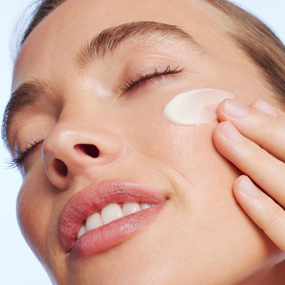 Una donna applica la crema Nuxe Merveillance Lift sulla sua guancia.