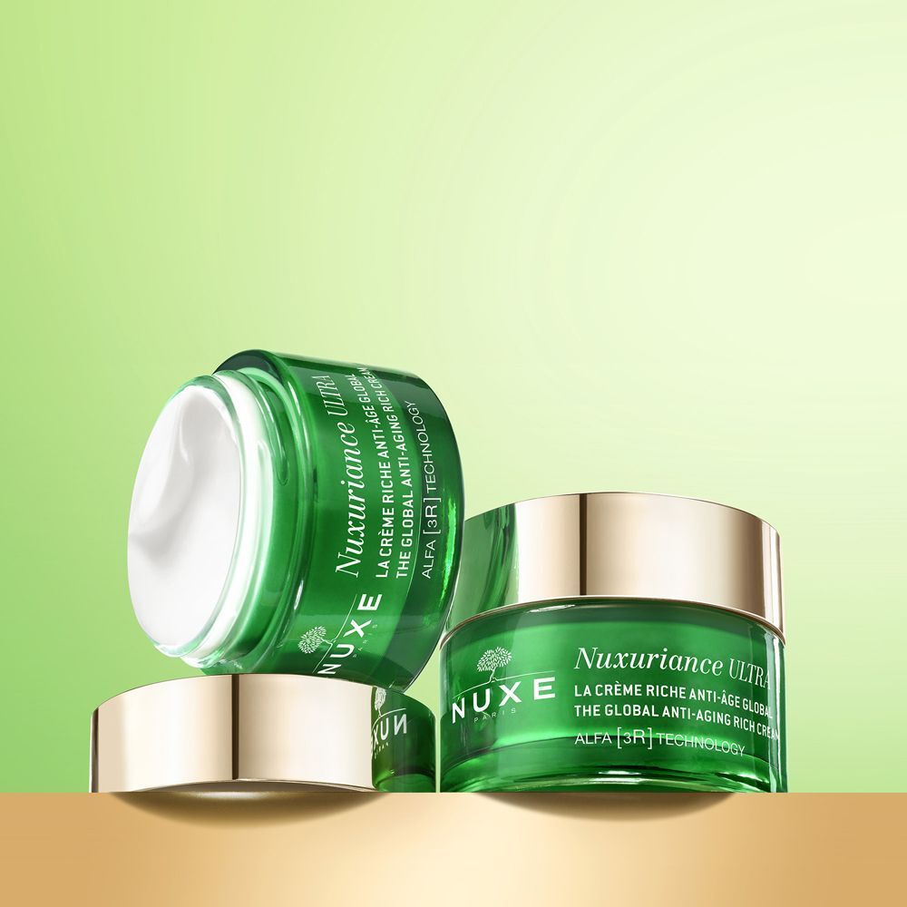 Tre vasi Nuxe Nuxuriance Ultra, uno aperto, su una superficie dorata.