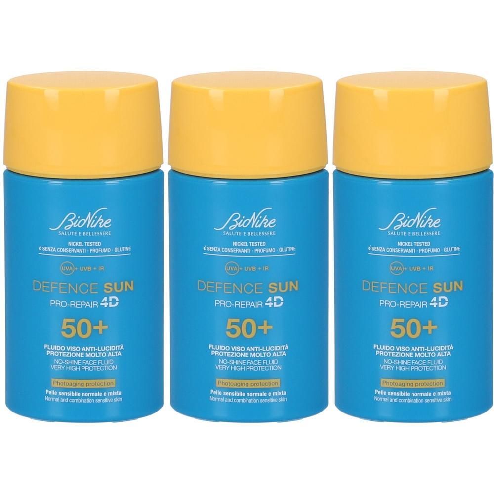 Tre flaconi blu con tappi gialli di BioNike Defence Sun Pro-Repair 4D SPF 50+ fluido viso.