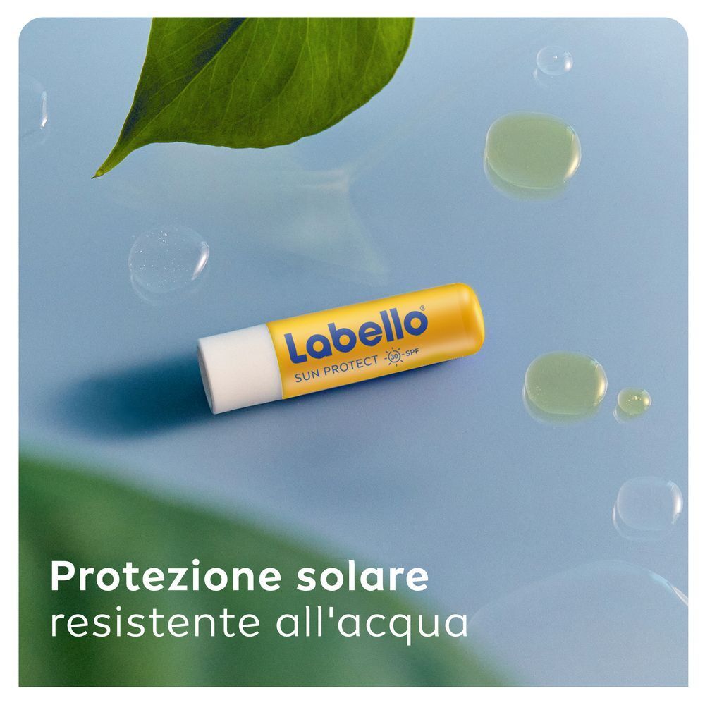 Balsamo labbra Labello Sun Protect SPF30 su sfondo blu con gocce d'acqua e foglia.
