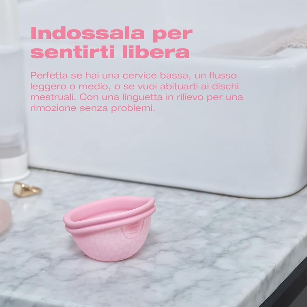 Coppetta mestruale rosa su superficie in marmo vicino a un lavandino.
