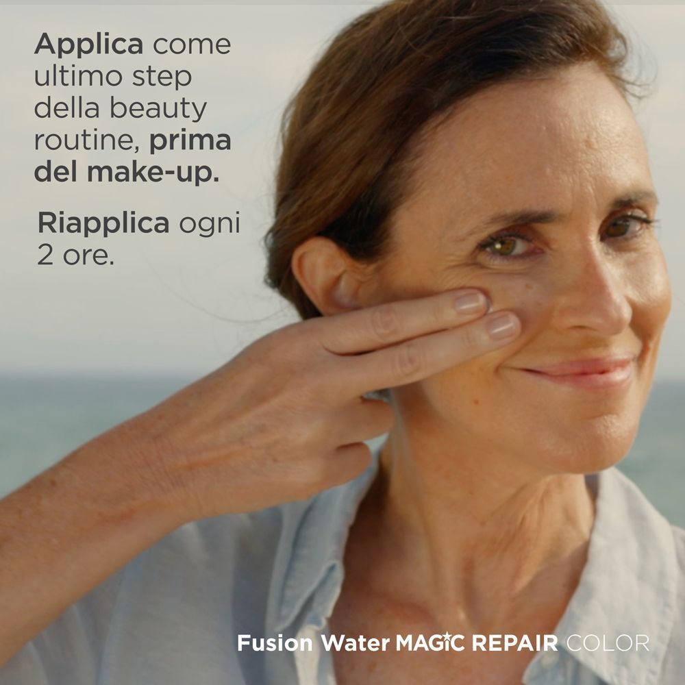 Una donna applica ISDIN Fusion Water Magic Repair Color Spray SPF 50 sul viso, con testo sull'applicazione.