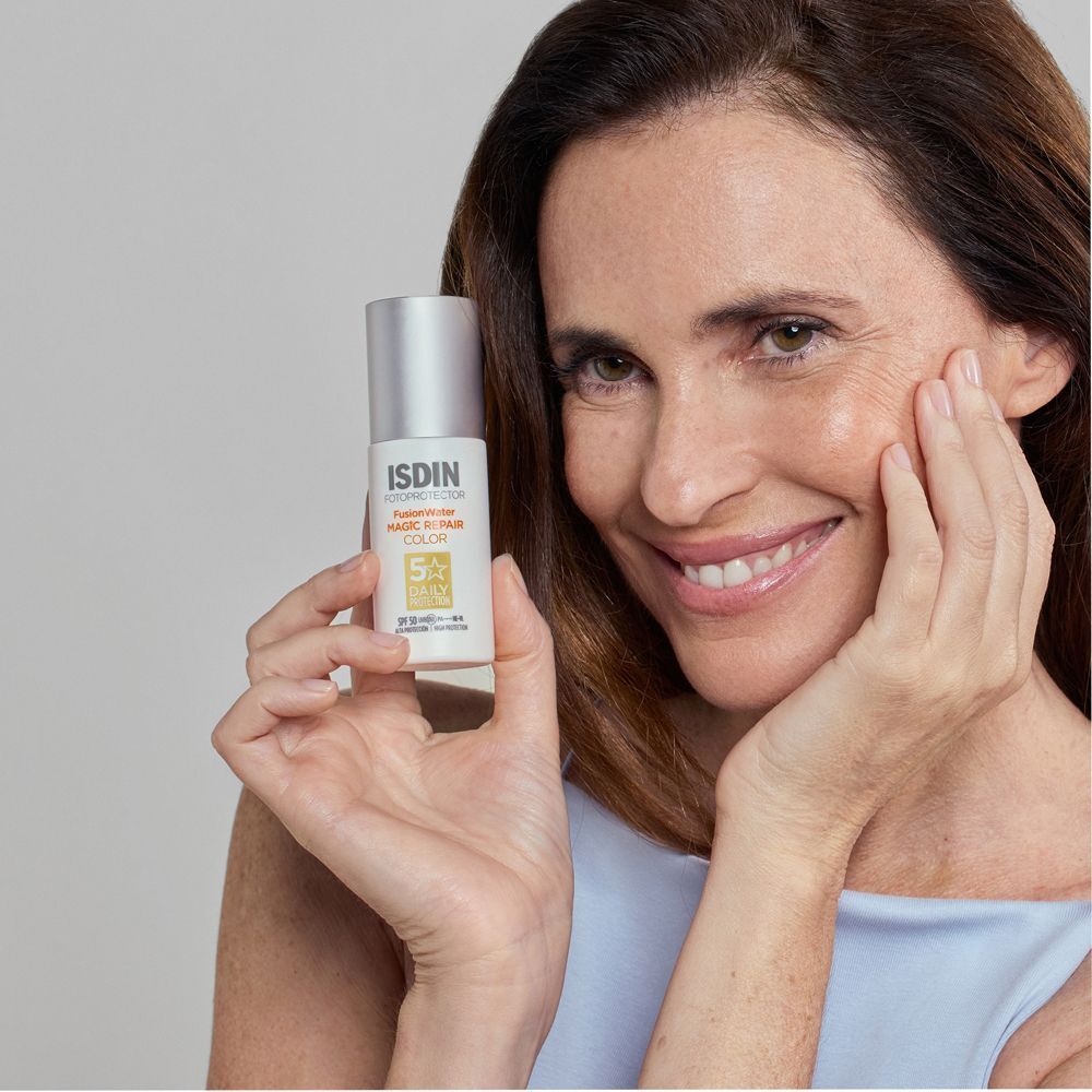 Una donna tiene un flacone di ISDIN Fusion Water Magic Repair Color Spray SPF 50 vicino al viso.