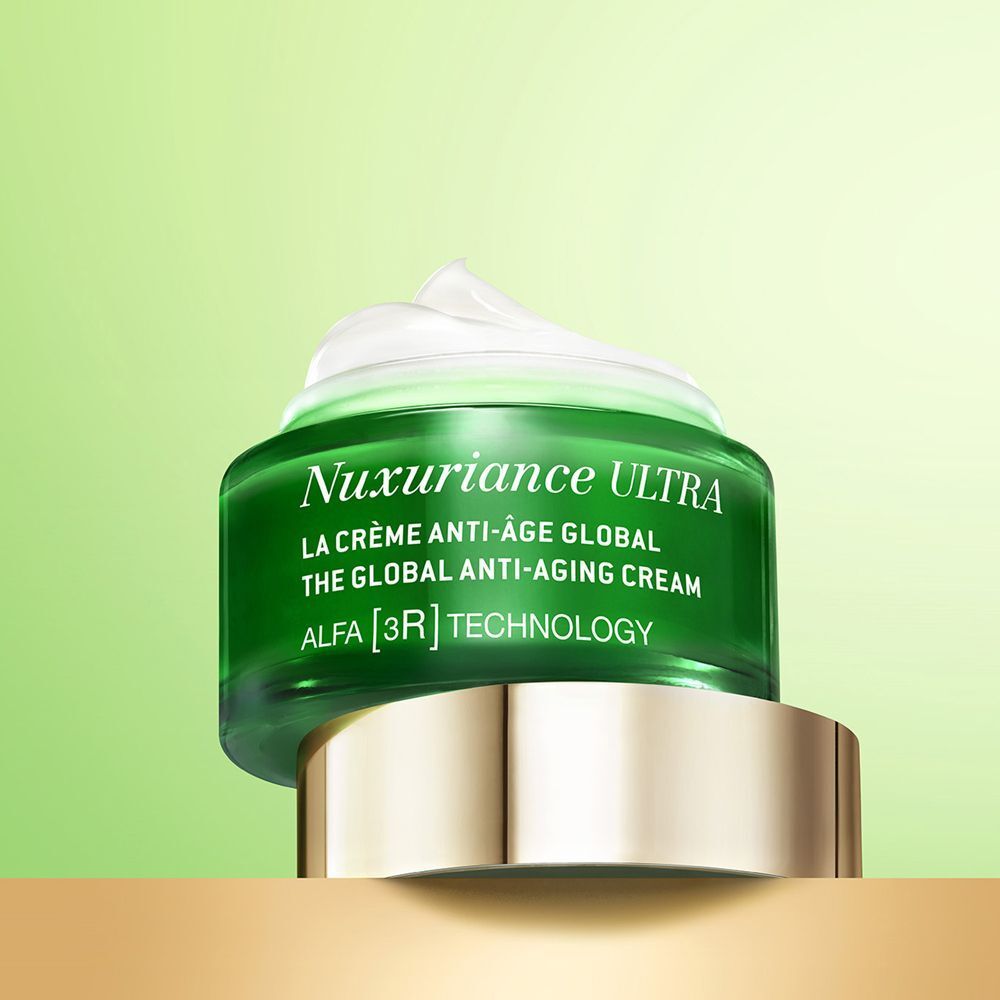 Un vasetto verde Nuxe Nuxuriance Ultra con crema anti-età su una base dorata.