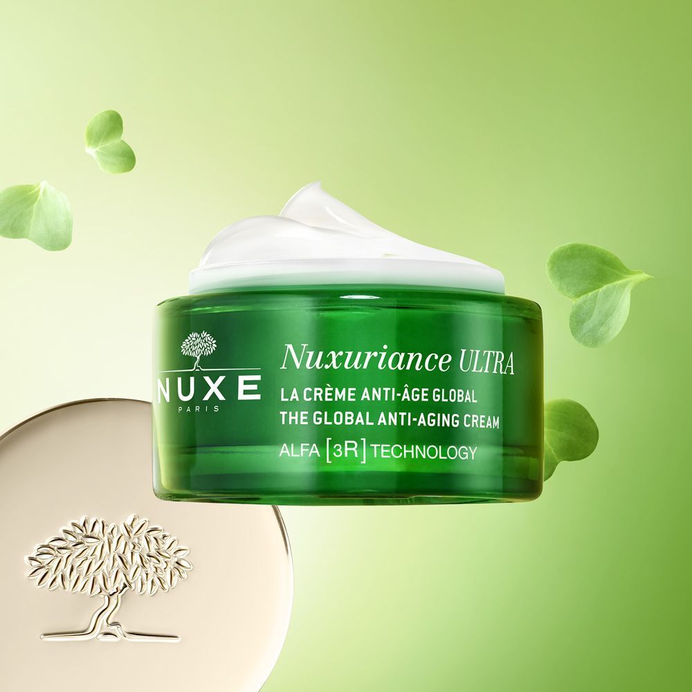 Un vasetto verde Nuxe Nuxuriance Ultra con crema, circondato da foglie verdi.