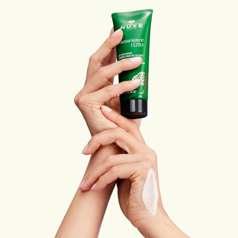 Mani che tengono un tubo di Nuxe Nuxuriance Ultra Crema Mani Correttore Macchie.
