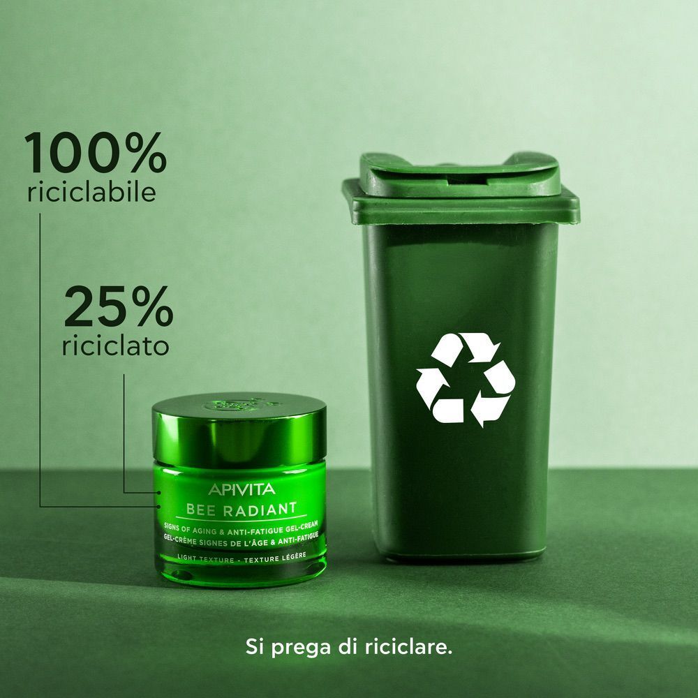 Vasetto verde di Gel-Crema APIVITA Bee Radiant accanto a un bidone verde per il riciclo.