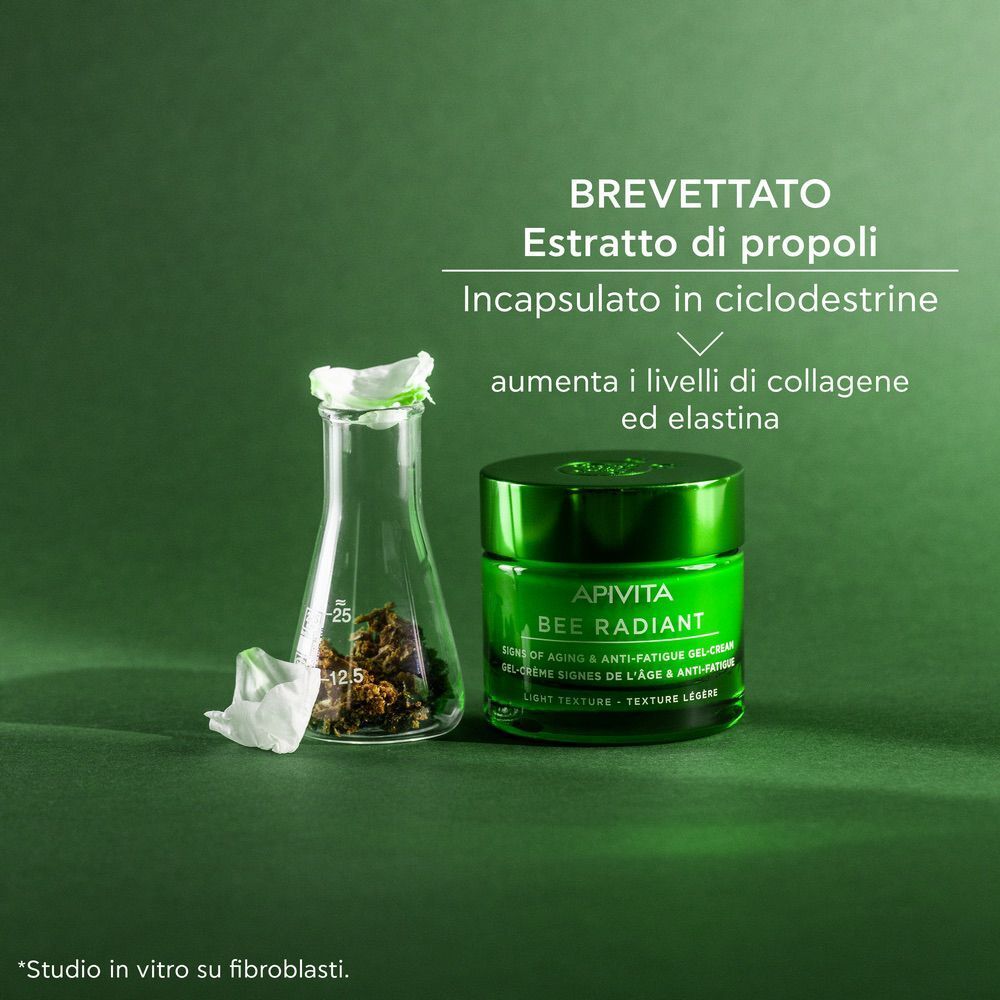 Vaso verde APIVITA BEE RADIANT crema viso accanto a un pallone da laboratorio con propoli.