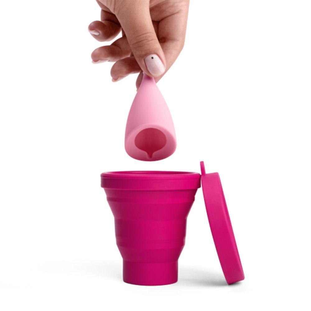 Una mano tiene una coppetta mestruale rosa sopra uno sterilizzatore pieghevole.